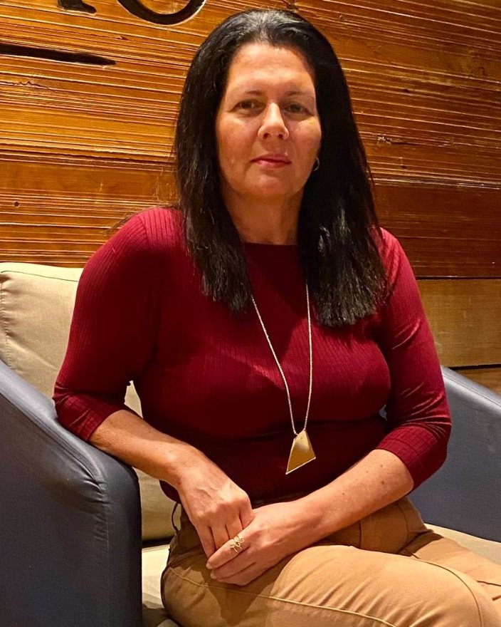Mariana Castilhos, fonoaudióloga, sentada, de blusa vinho.